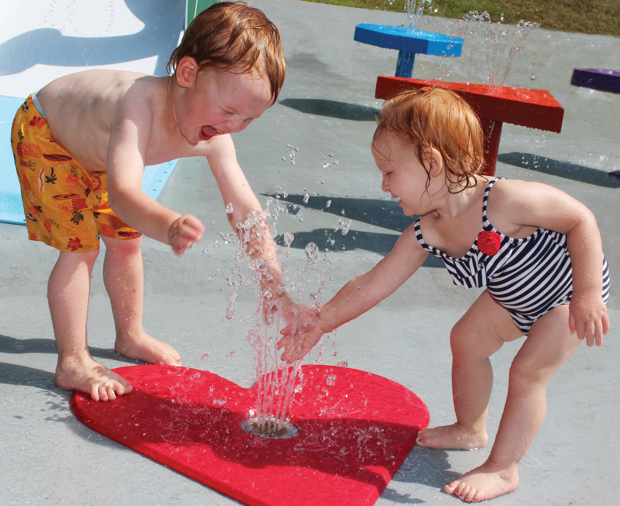 Two toddlers playing with heart-shaped commercial water park equipment.