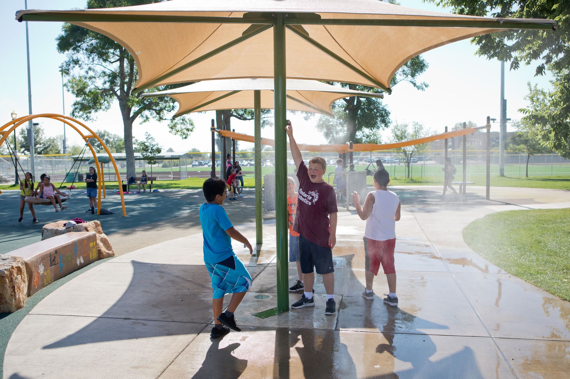 Three boys playing under misting commercial water park equipment.