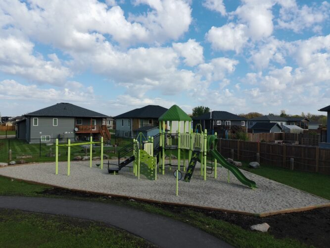 Playground structure at Amberfield Park in Manitoba, with neighborhood homes nearby.